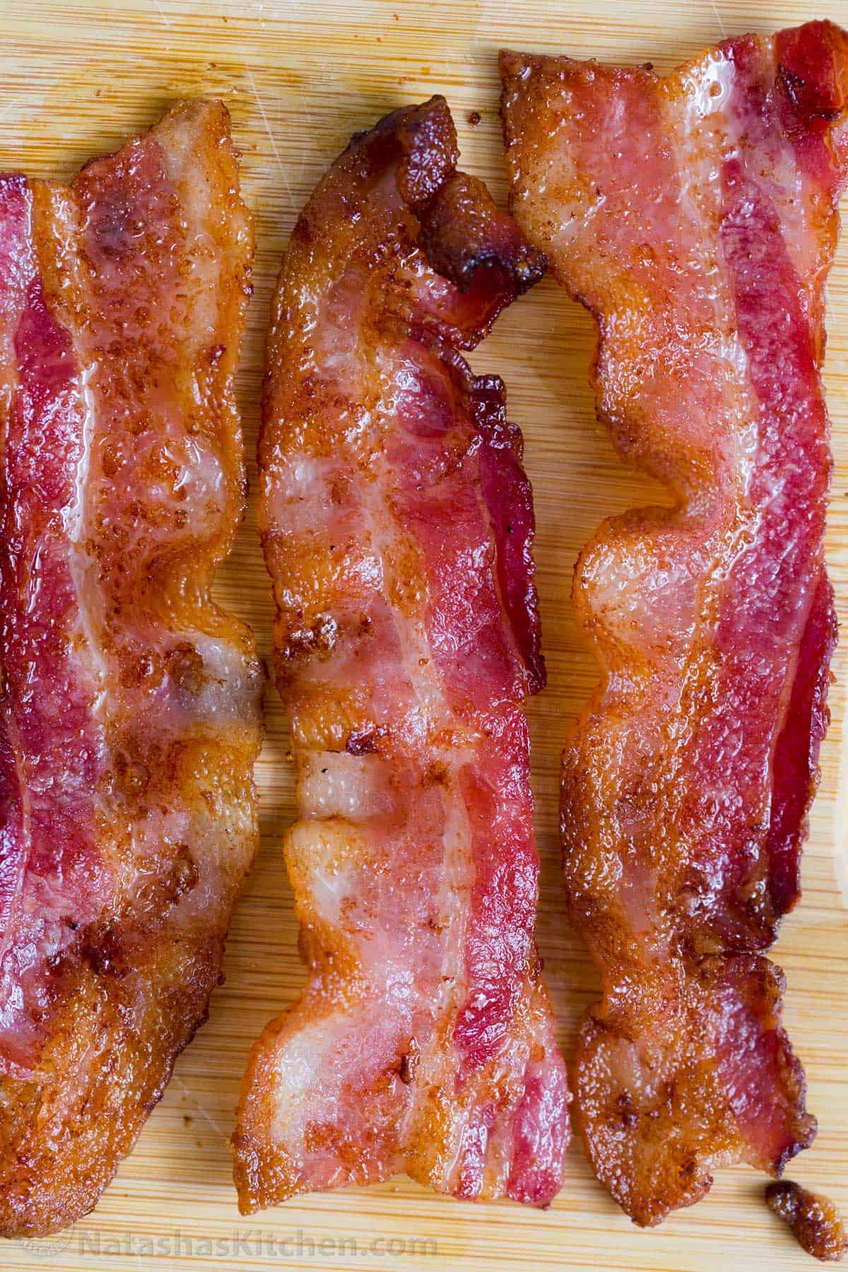 Three slices of crispy cooked bacon laid out on a cutting board. 