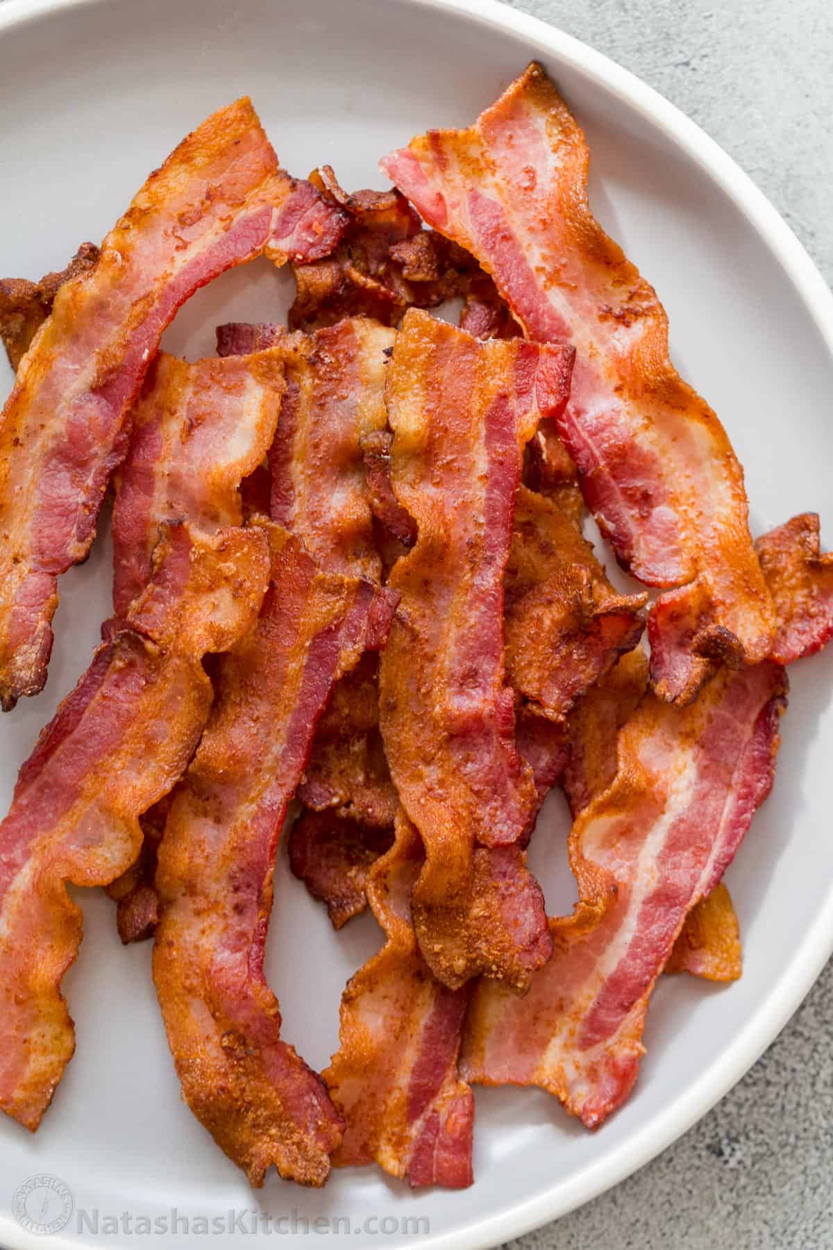 Crispy air fryer bacon on a white plate stacked on top of each other. 