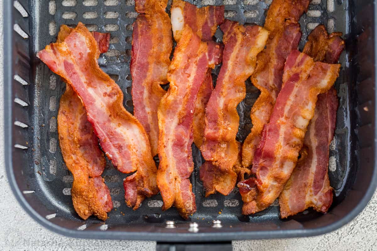 Crunchy bacon strips laid out in an air fryer basket. 
