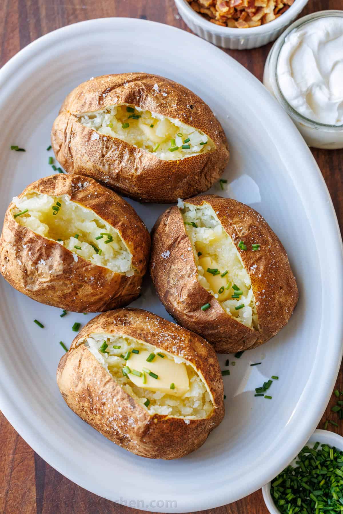 Air fryer baked potatoes served on white platter with butter and chives