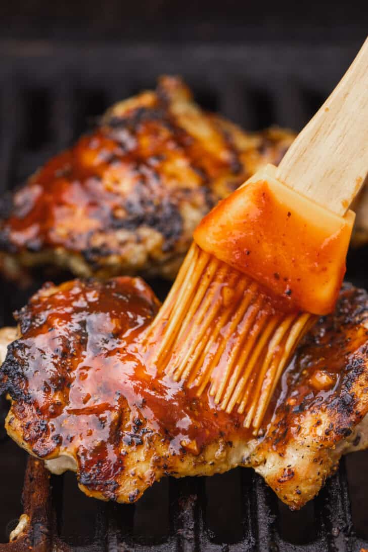 Brushing BBQ sauce onto chicken while it grills