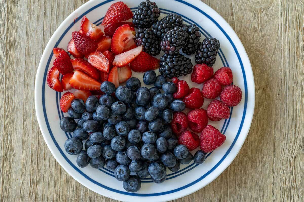 cut strawberries, blackberrries, raspberries and blueberries on a white and blue plate