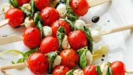 Caprese skewers recipe with tomatoes, basil, mozzarella pearls and balsamic glaze on a white plate