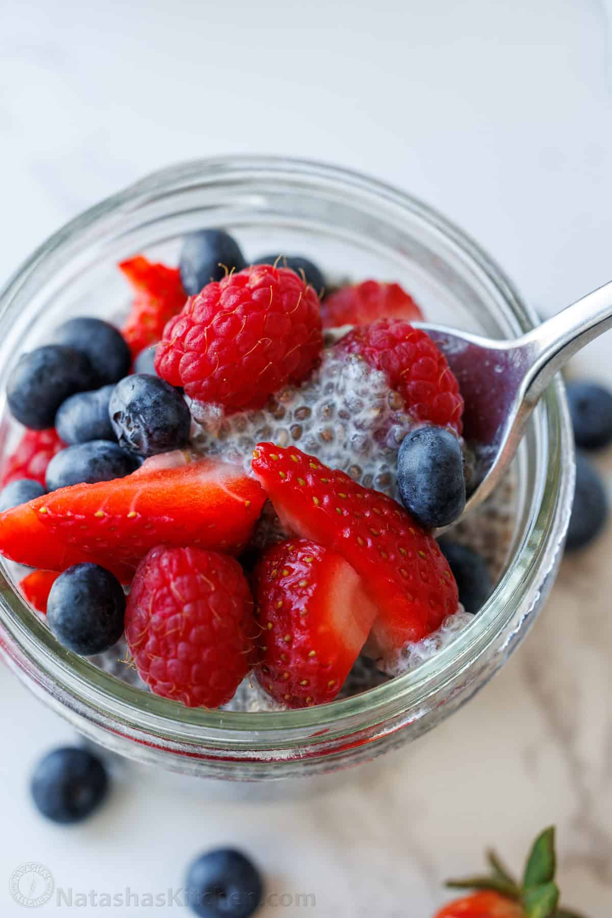 a spoon scopping chia seed pudding out of a mason jar with berries on top