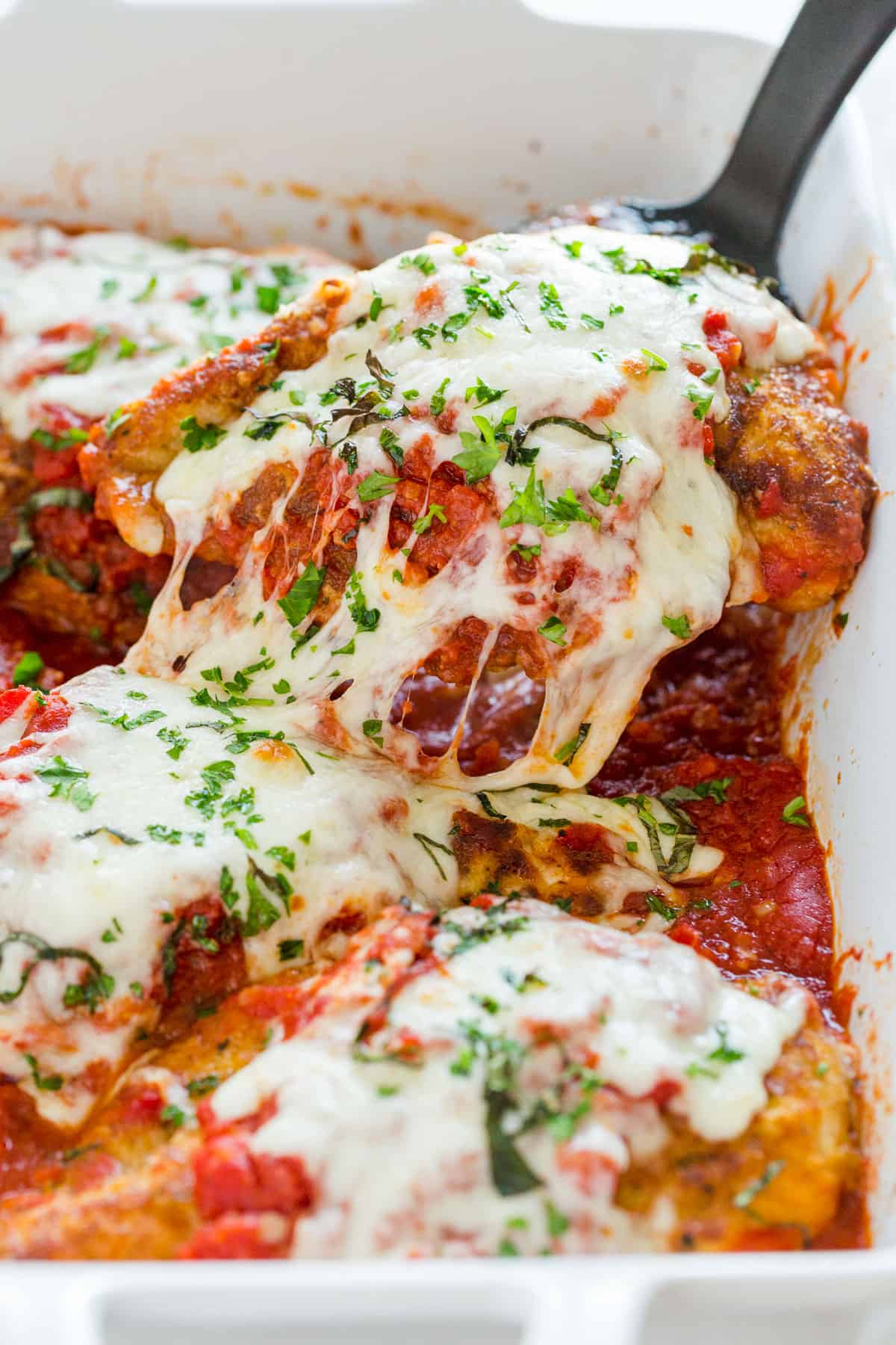 Chicken Parmigiana being served out of a casserole dish with spatula and cheese pull