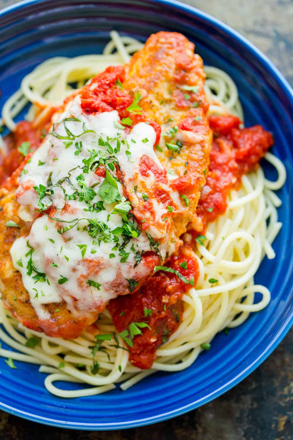 Chicken Parmesan served over pasta and marinara sauce, garnished with parsley