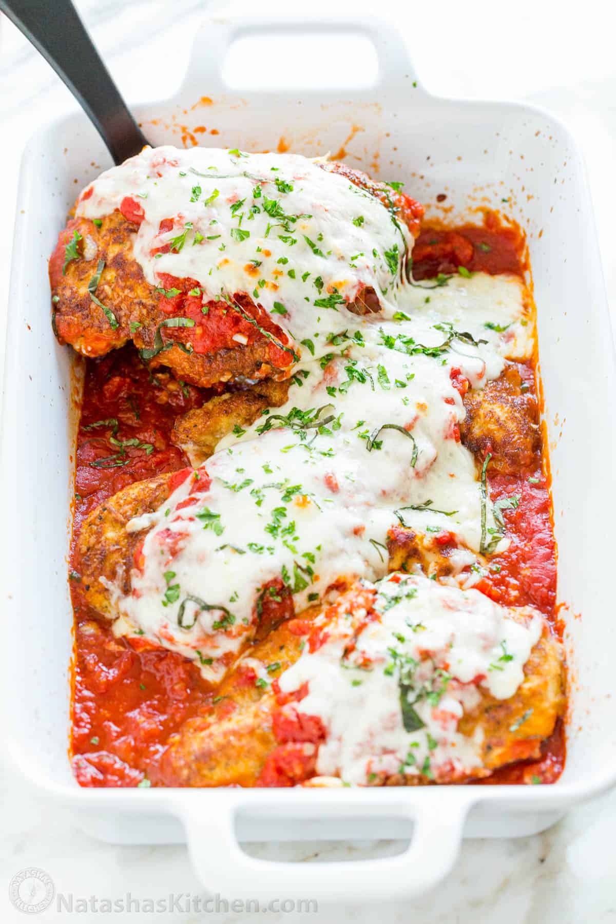 Chicken parmesan served out of white casserole dish with spatula