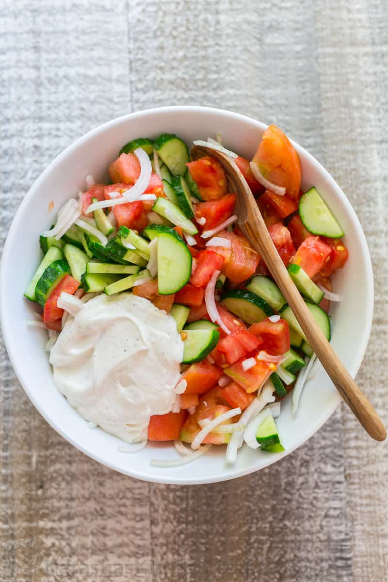 tomato cucumber salad in a white bowl with salad dressing on top
