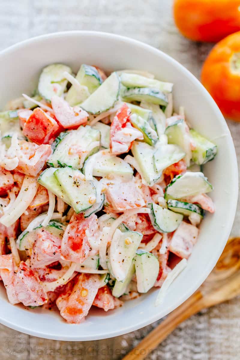 Classic cucumber tomato salad with creamy dressing in a white bowl with fresh tomatoes