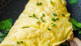 Omelette cooked in a skillet with spinach and mushrooms