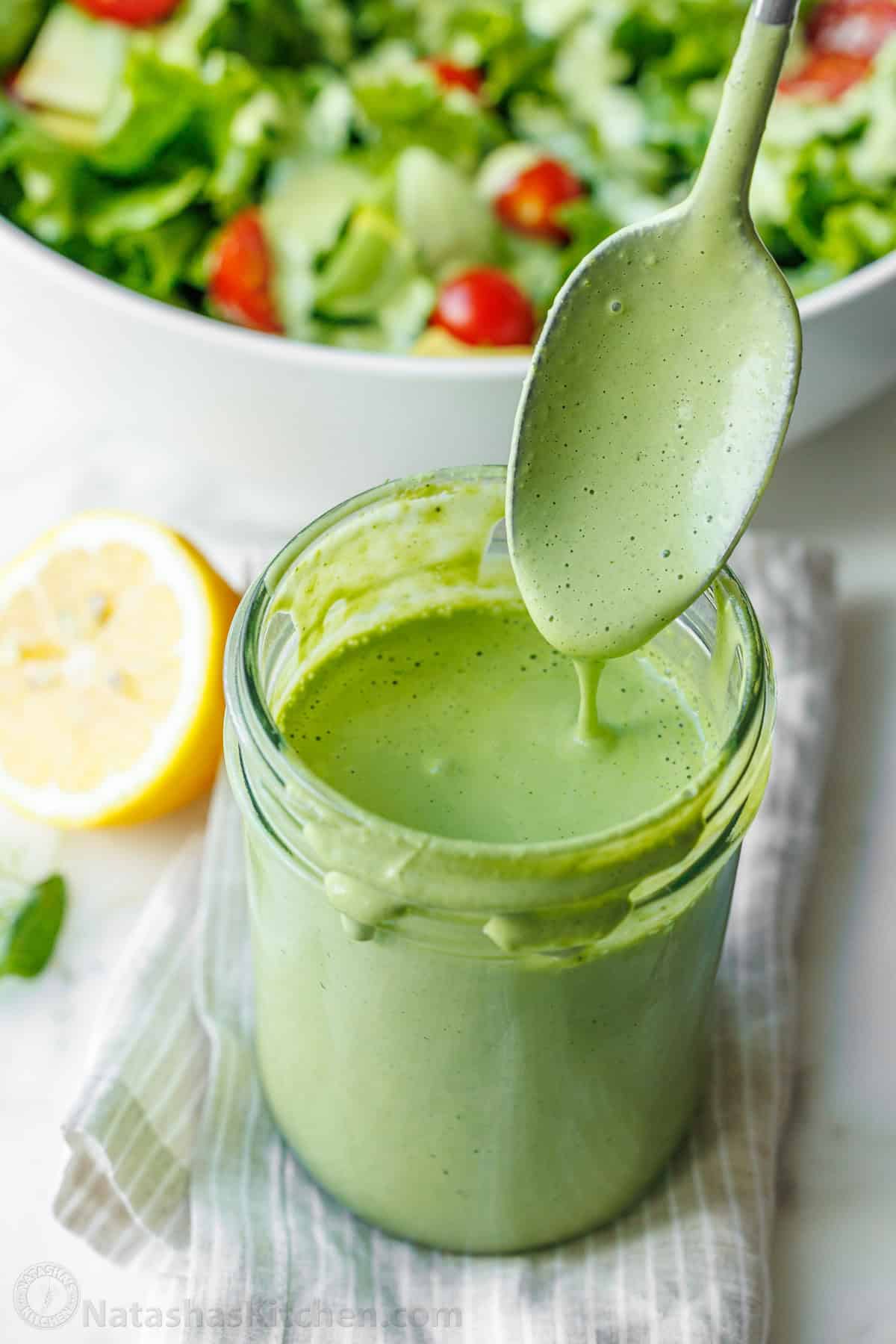 A spoon serving Green Goddess salad dressing from a mason jar onto a mixed green salad
