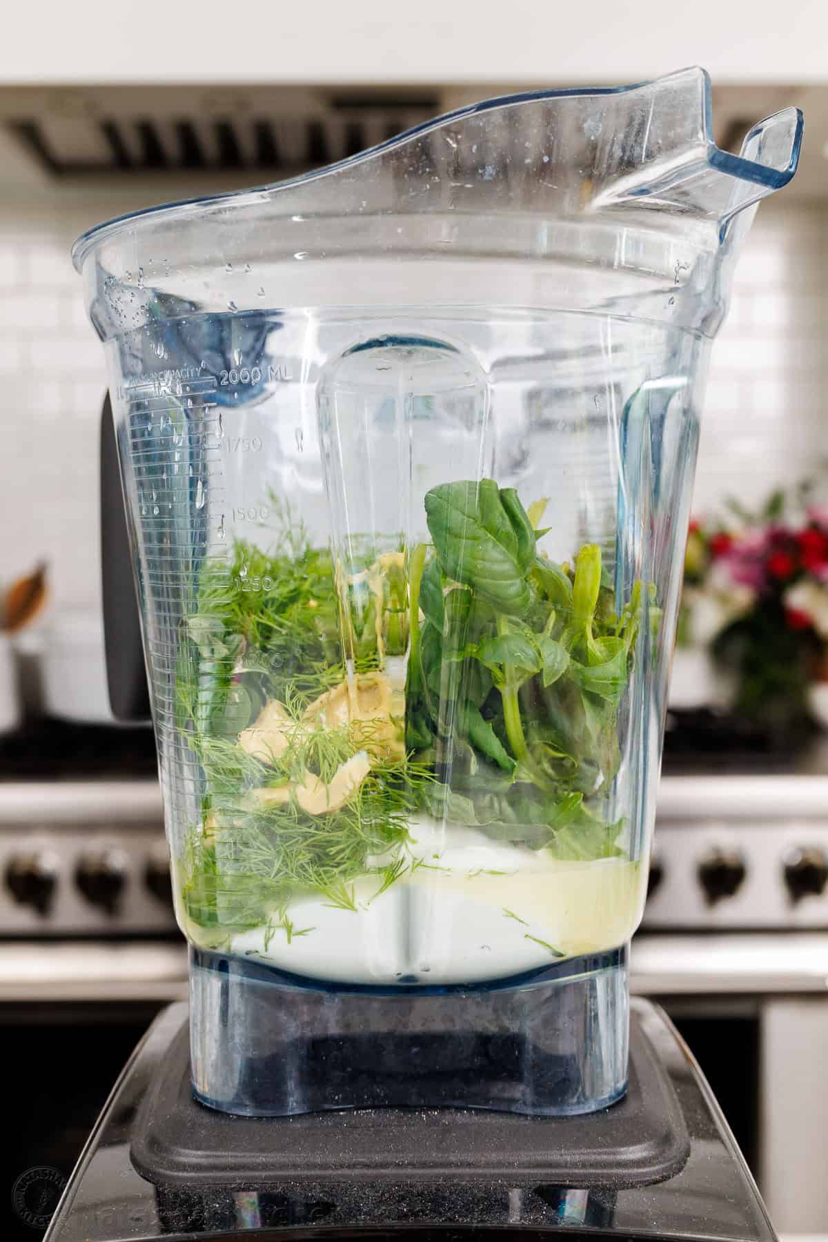 Ingredients for Green Goddess Dressing in a blender including fresh herbs, Greek Yogurt, seasoning, and mustard