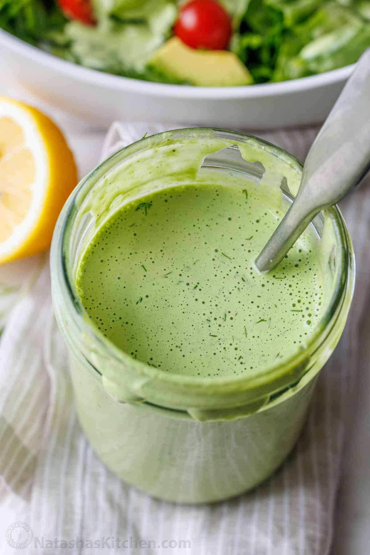 Green Goddess Salad Dressing in a mason jar mixed with a spoon and dotted with tiny specs of dill.