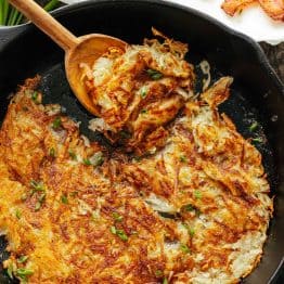 Hash browns in a cast iron skillet with a serving spoon