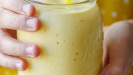 hands holding a yellow mango smoothie in a mason jar with yellow polka-dot background