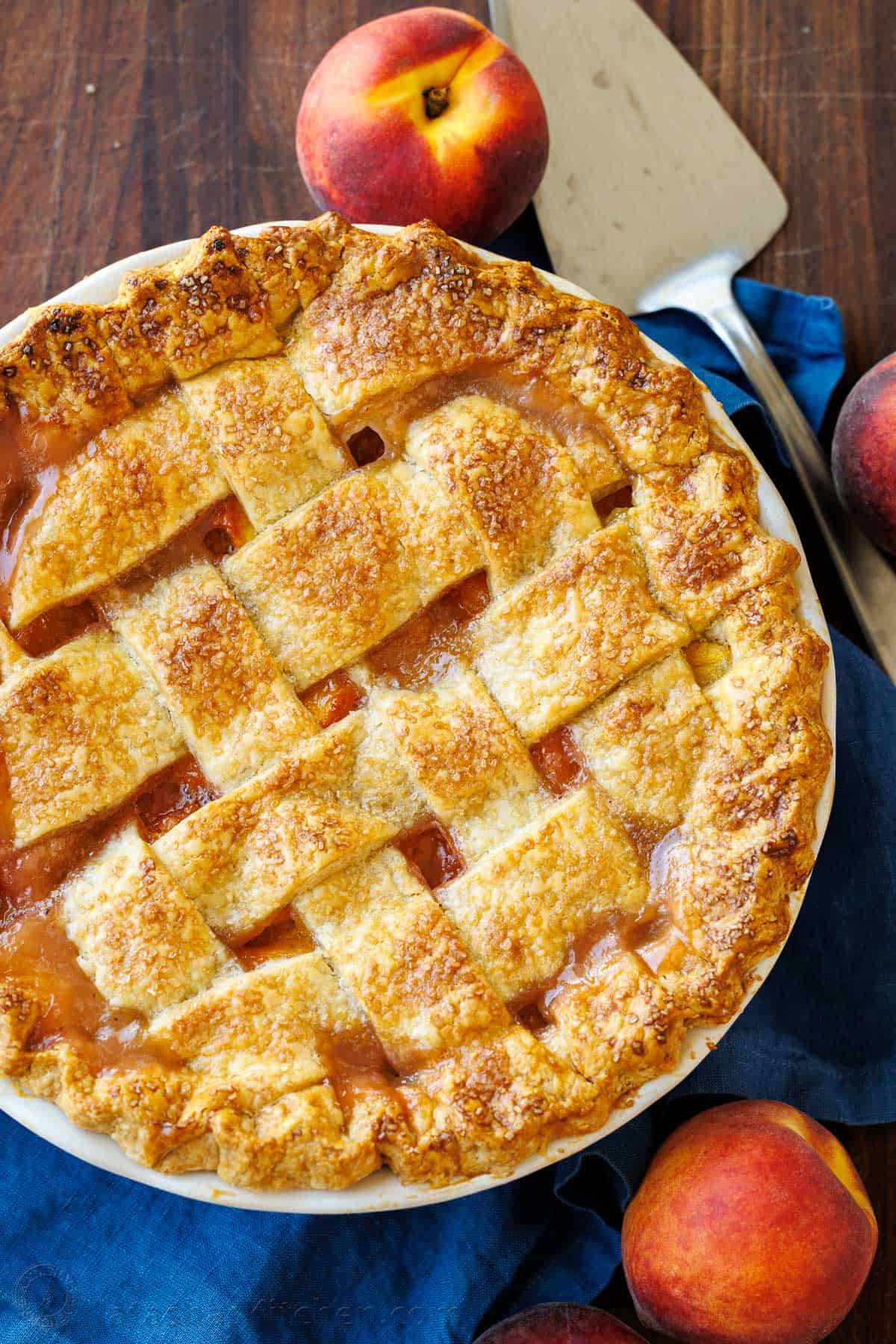 Peach Pie recipe with lattice crust on a blue table cloth with a pie server.