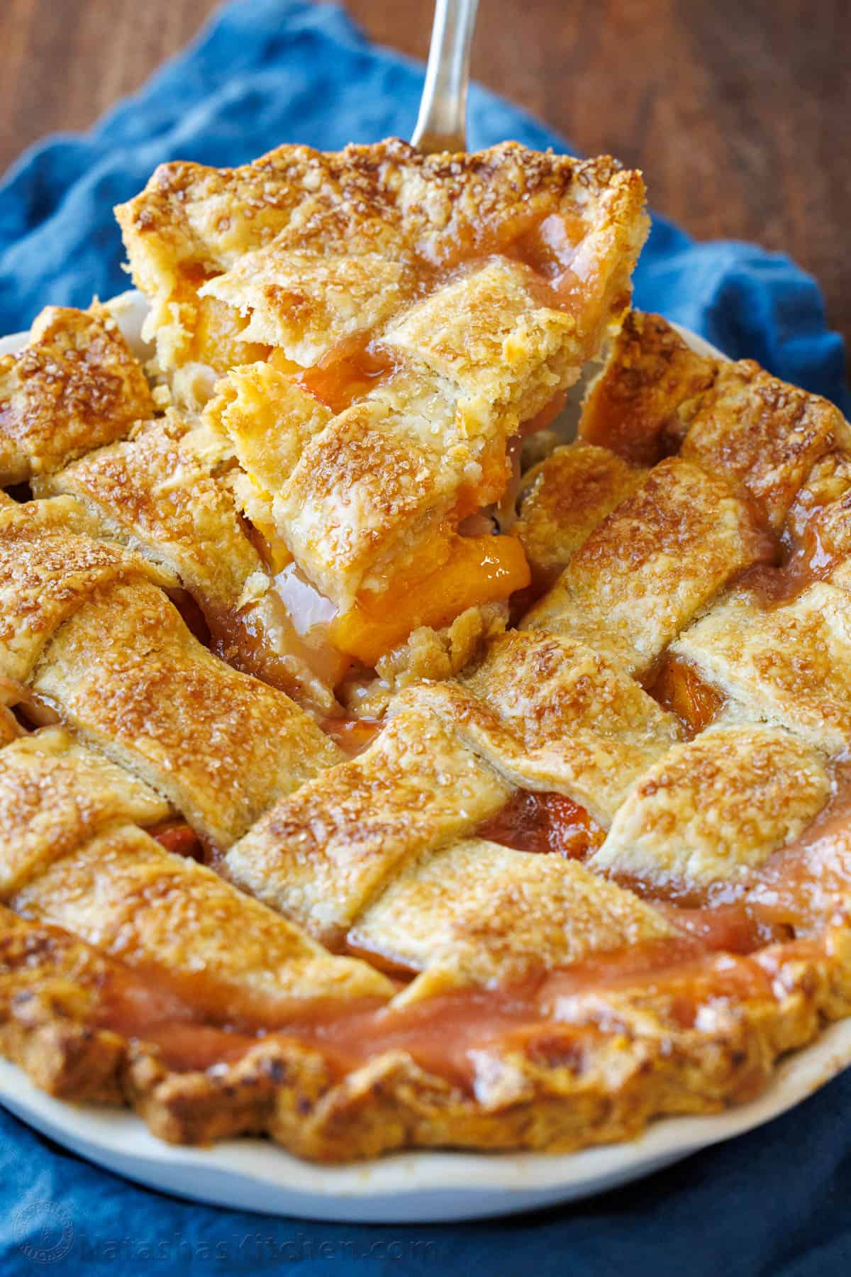 Slice of peach pie lifting out of the dish with blue napkin