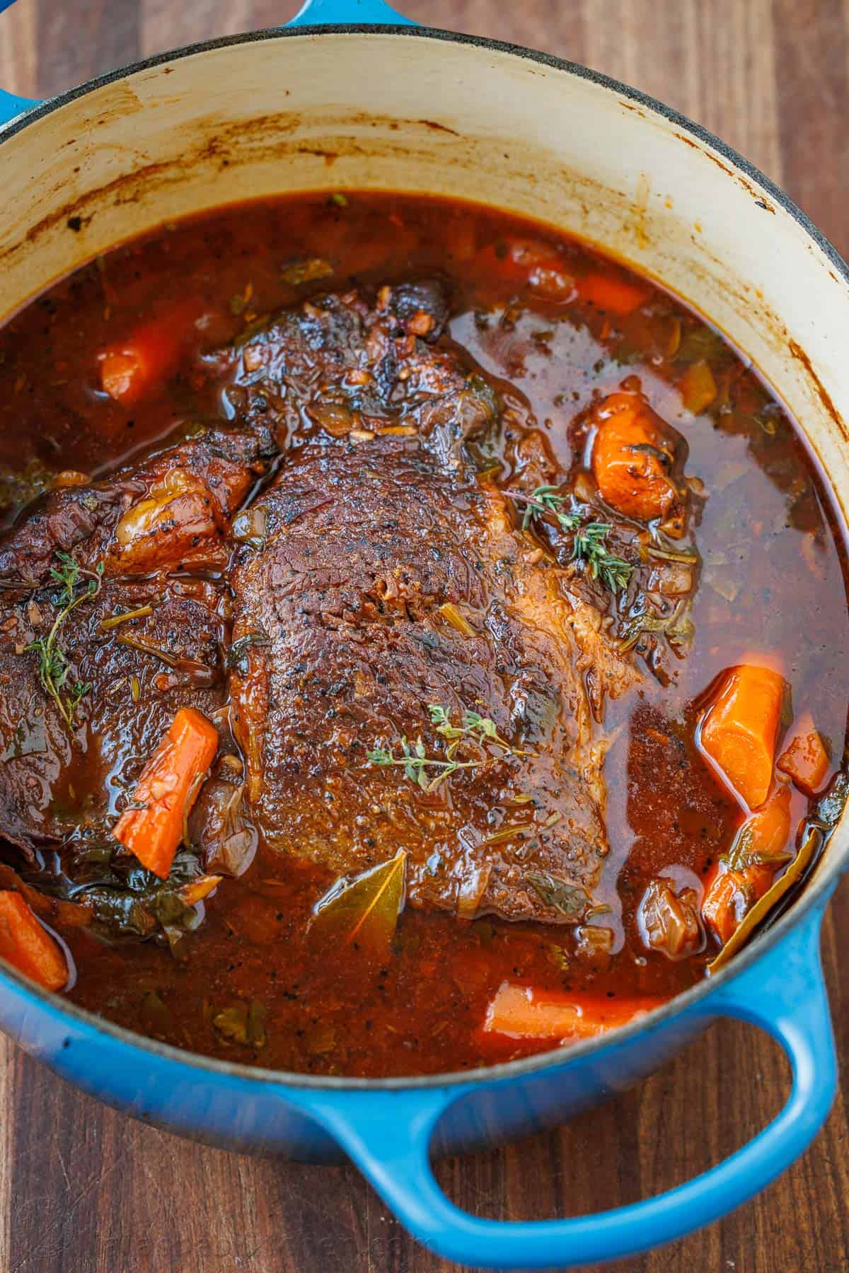 Chuck pot roast in a blue dutch oven with carrots and herbs