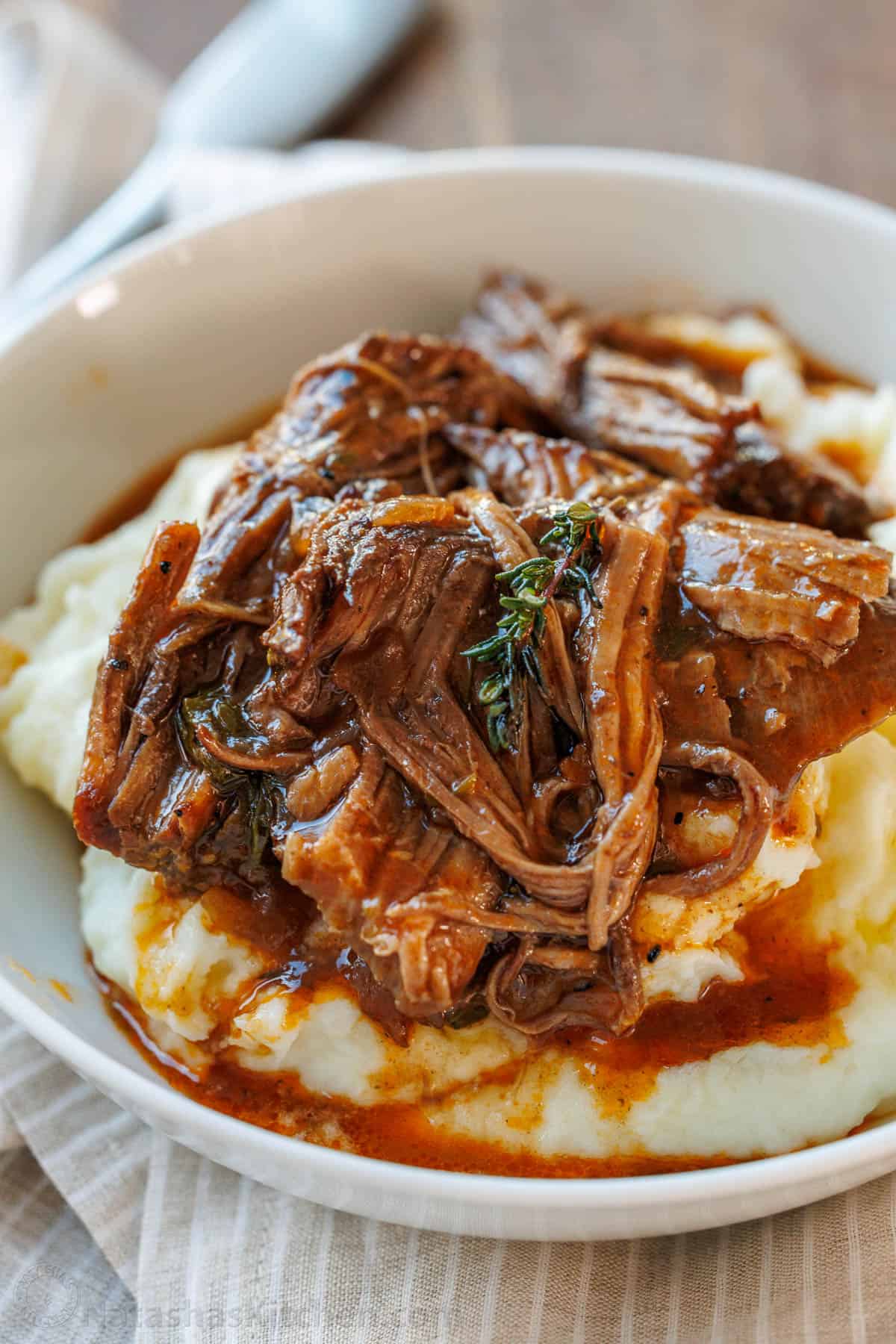 classic pot roast recipe served over mashed potatoes in a white bowl