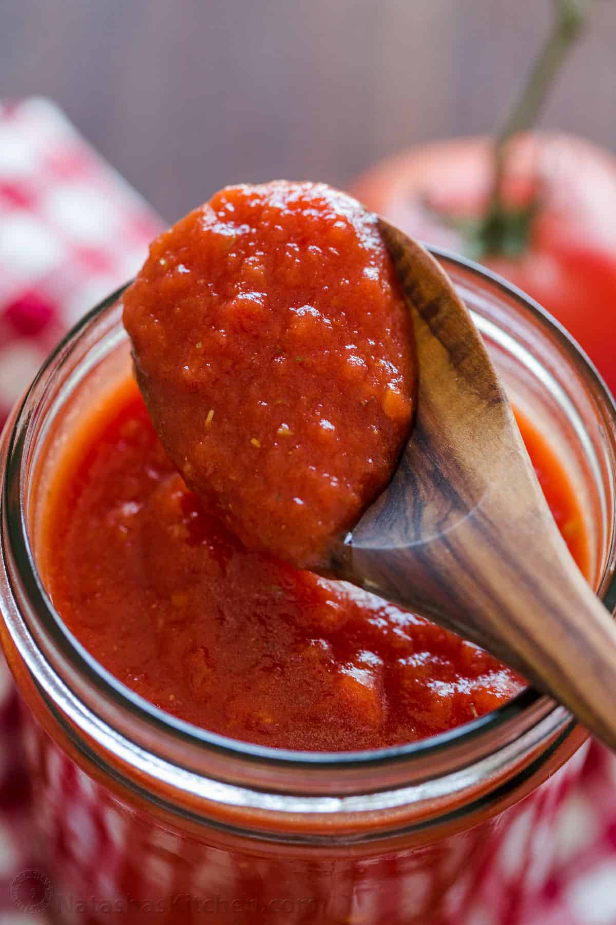 spoon scooping tomato sauce over a mason jar