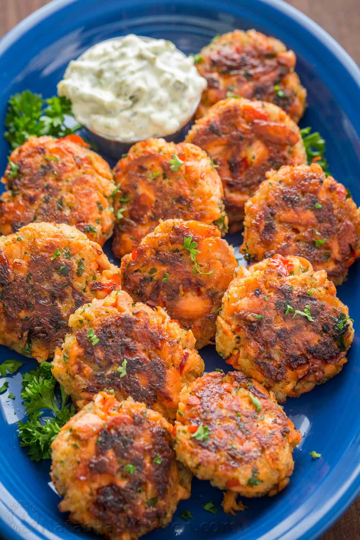 fish patties on a blue platter with dipping sauce and parsley