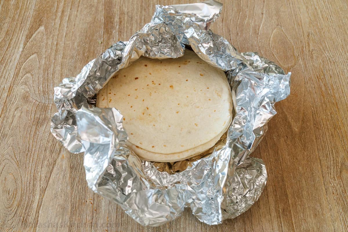 tortillas wrapped in foil on a wooden table to keep warm
