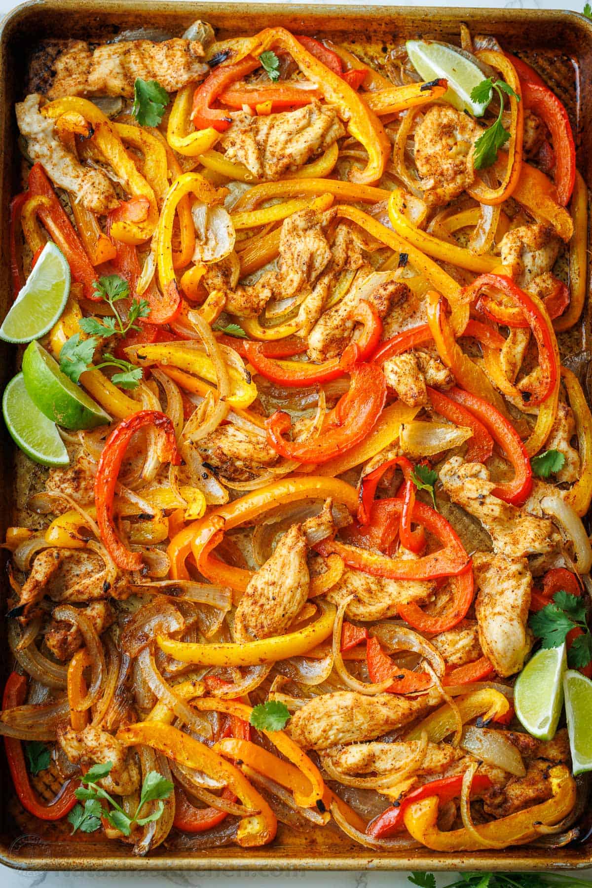 Sheet Pan Fajitas spread onto a cookie sheet with lime wedges and cilantro