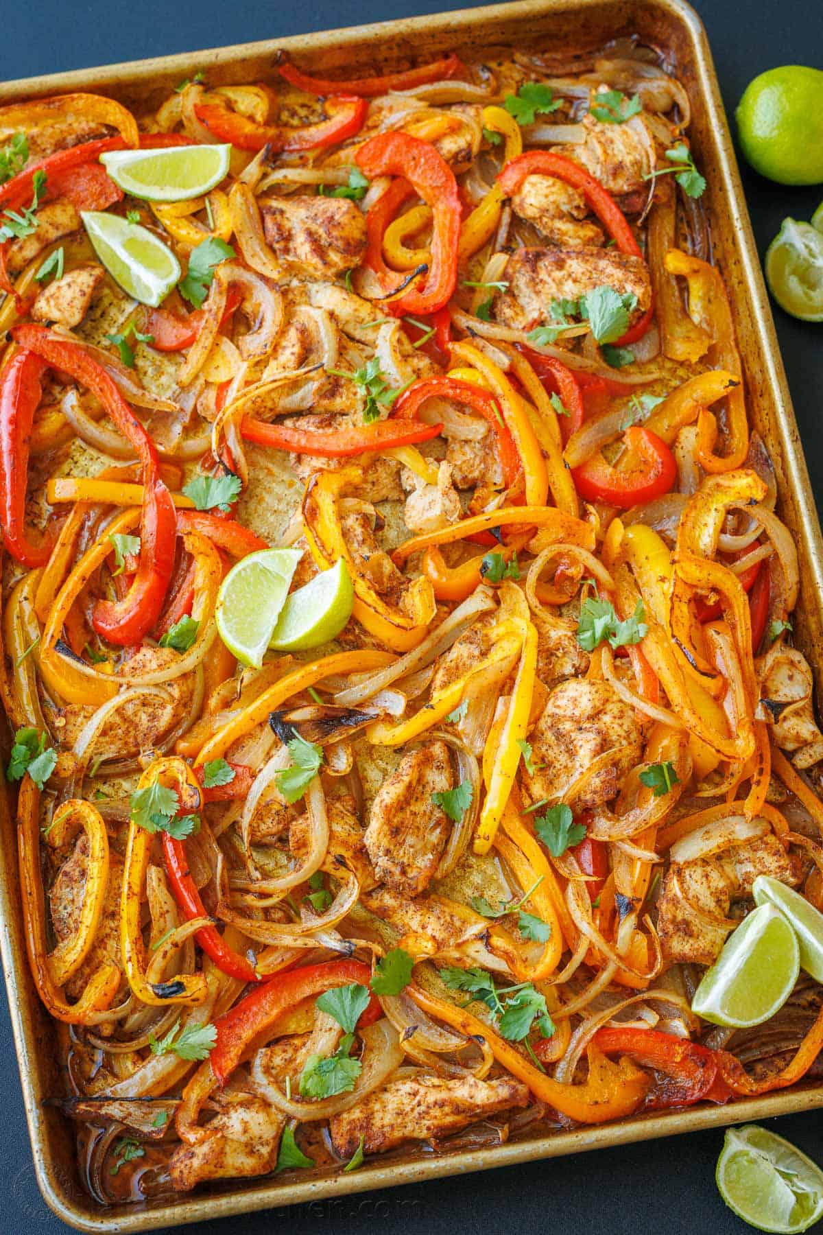 Chicken Sheet Pan Fajitas with peppers, lime wedges, chicken and homemade fajita seasoning