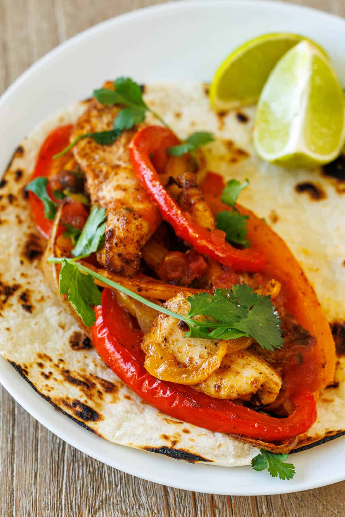 Mexican chicken fajita on a white plate with lime and cilantro to garnish