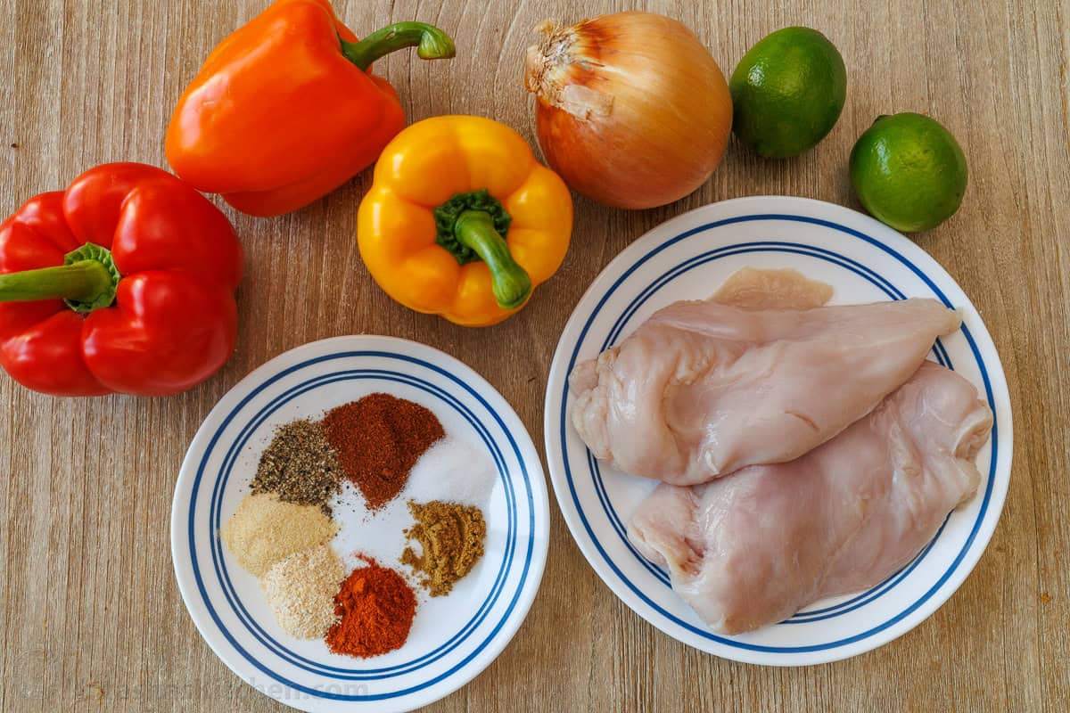 ingredients for sheet pan fajitas including chicken, bell peppers, onion, lime, and homemade fajita seasoning