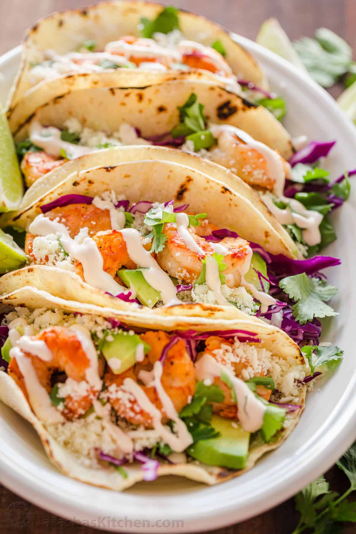 My easy Shrimp Tacos are loaded with shrimp, cabbage slaw, cotija cheese, and the BEST garlic-lime crema sauce. It's the only recipe you need! easy Shrimp tacos on a platter drizzled with garlic-lime crema shrimp taco sauce