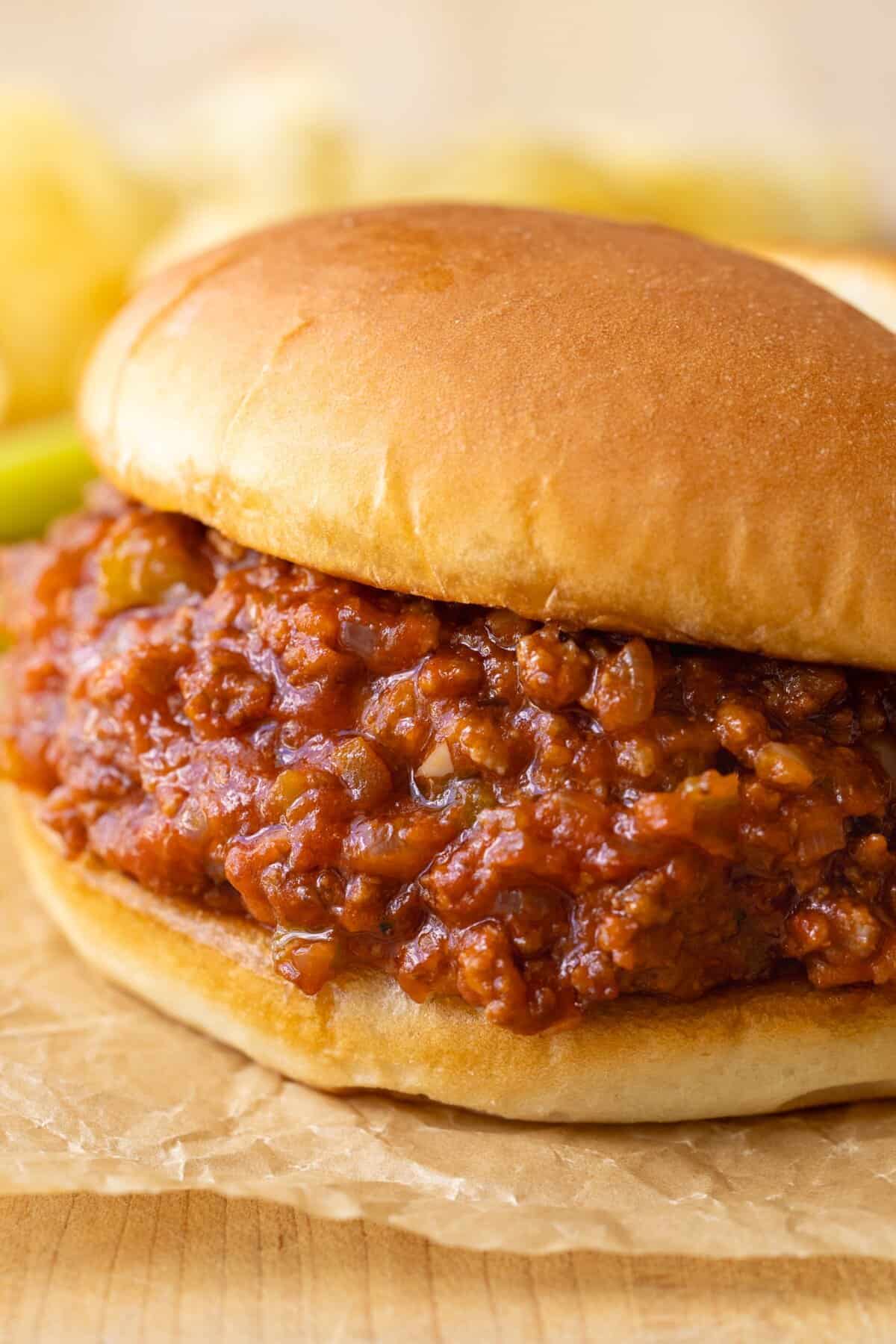 Sloppy Joe up close with saucy sloppy joe filling on a bun served with pickles and chips