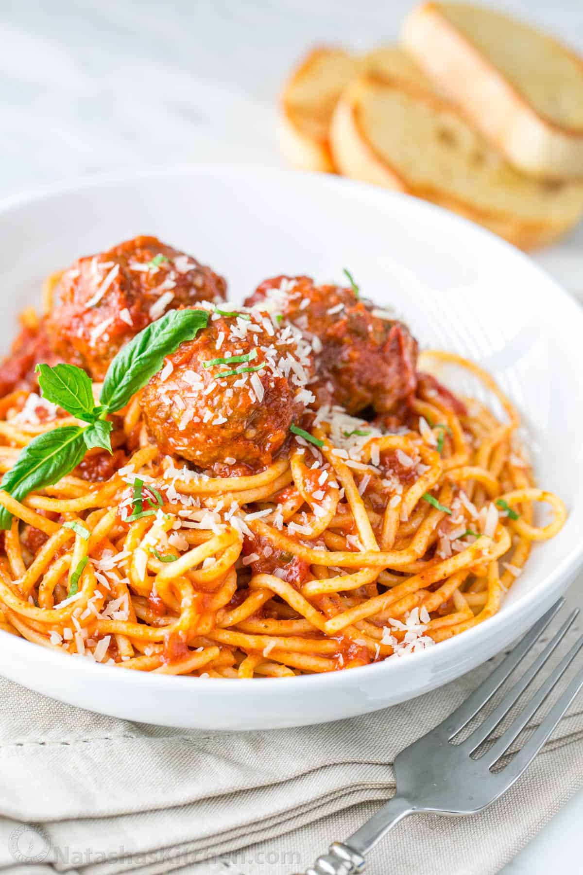 Spaghetti and meatballs served on a white plate garnished with parmesan cheese and served with a fork