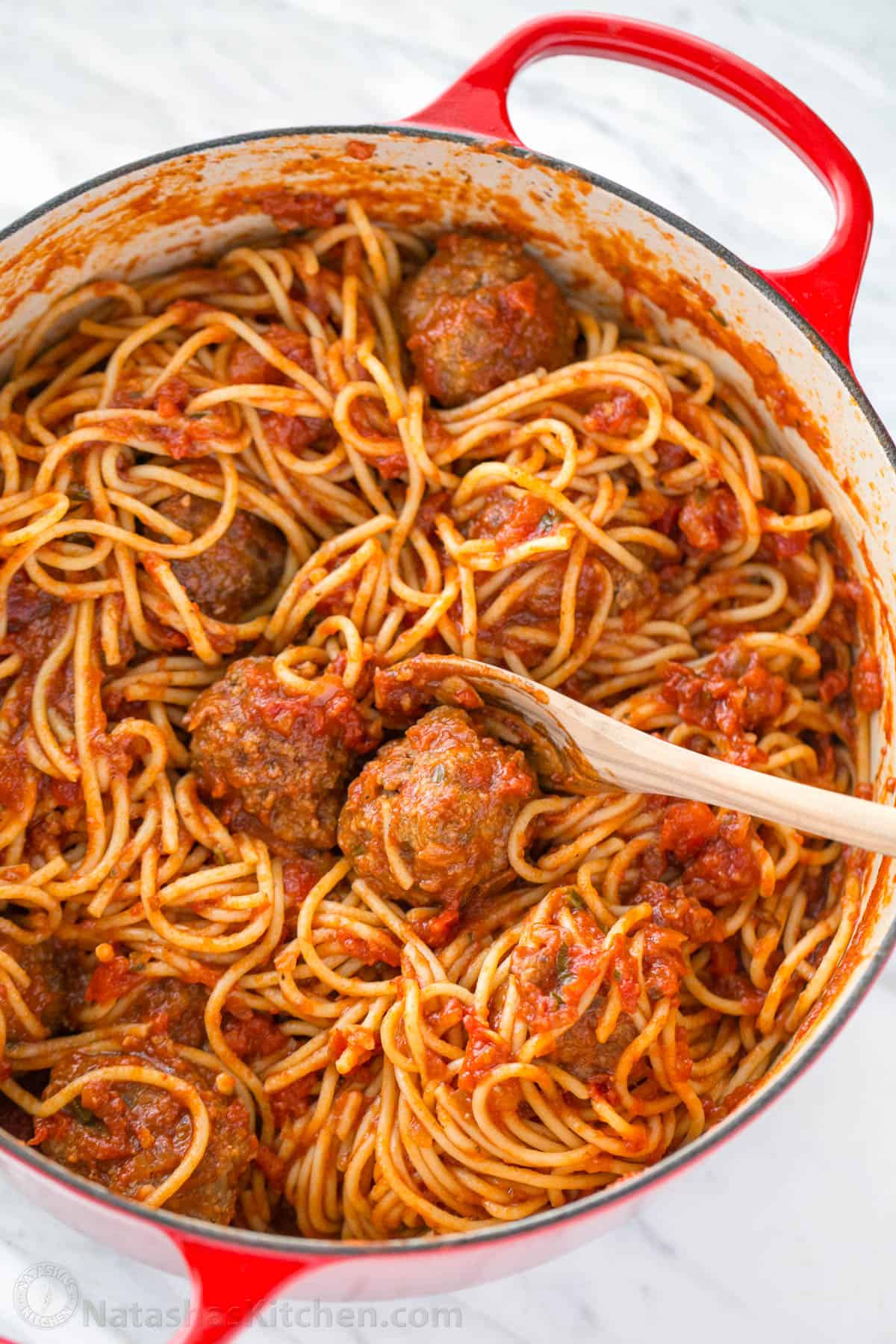 Spaghetti and Meatballs tossed together with sauce in a red dutch oven pot. 