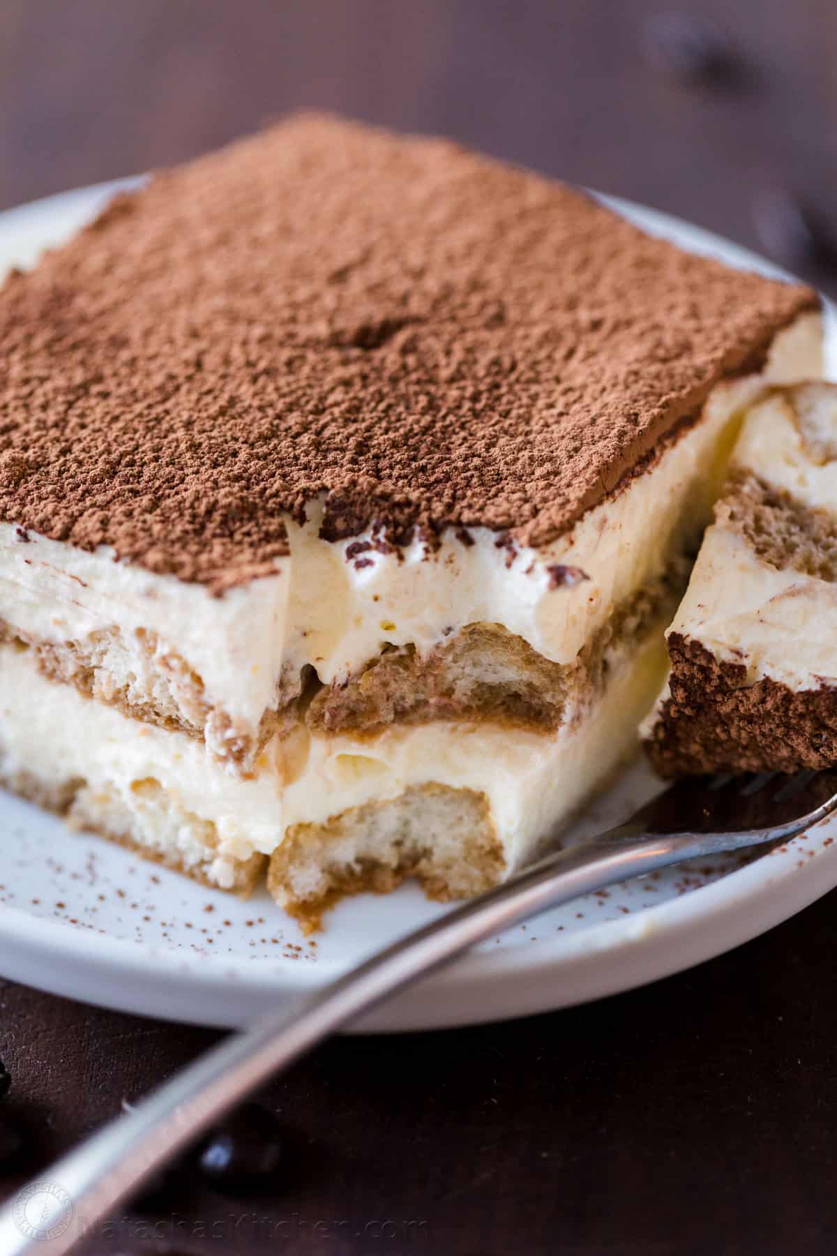 a slice of homemade tiramisu cake on a plate with a bite taken out of the corner with a fork